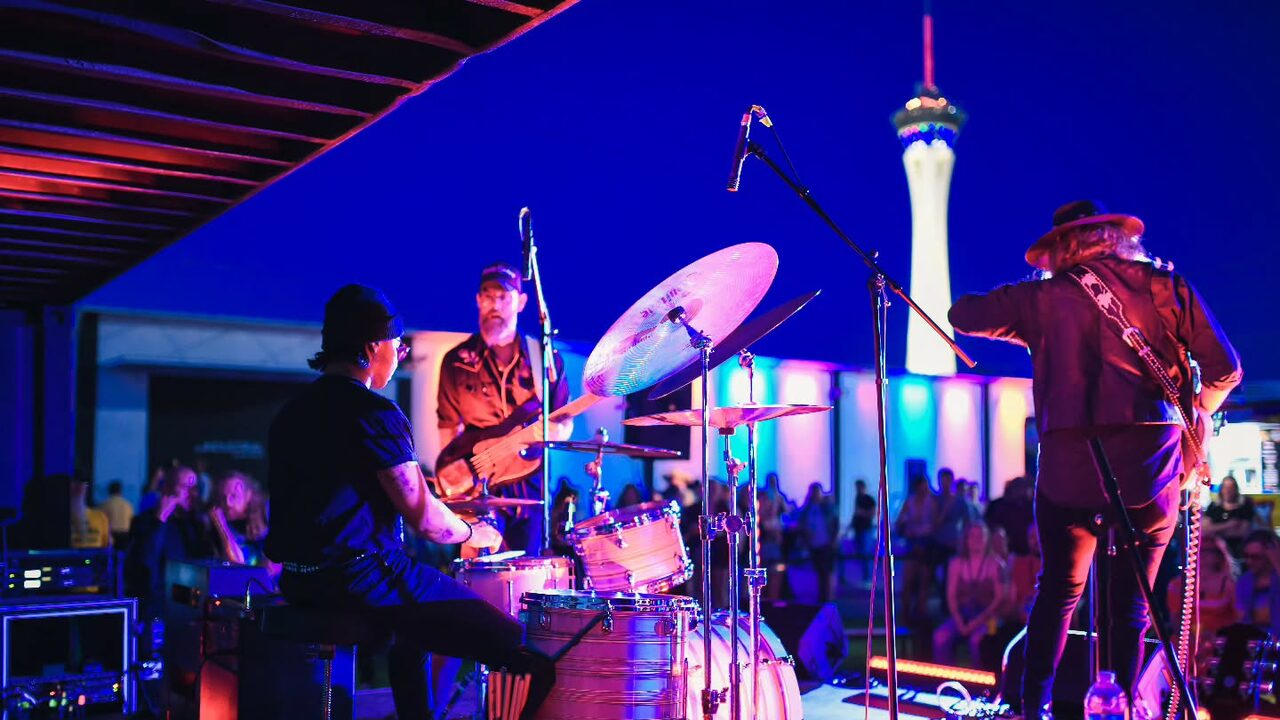 Musicians performing under blue and pink outdoor stage lights